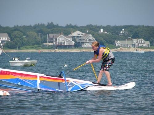 kobieta trenująca windsurfing podnosi żagiel z wody stojąc na desce